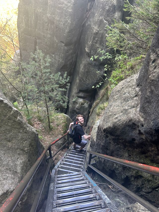 Fynn Ellie climbing down steep metal stairs into a ravine in the Elbe Sandstone Mountains, tall cliff-like rocks to the left and right.