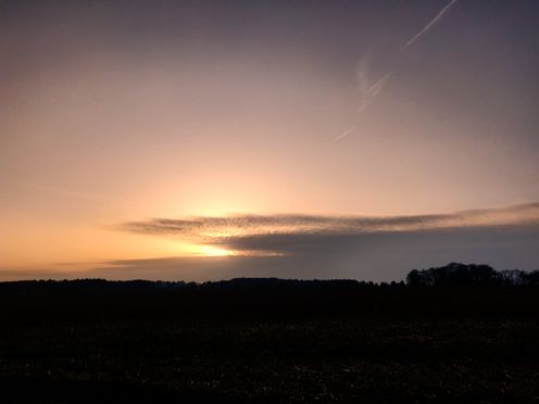 Dark landscape under a golden sky lit by a setting sun partly obscured by clouds.