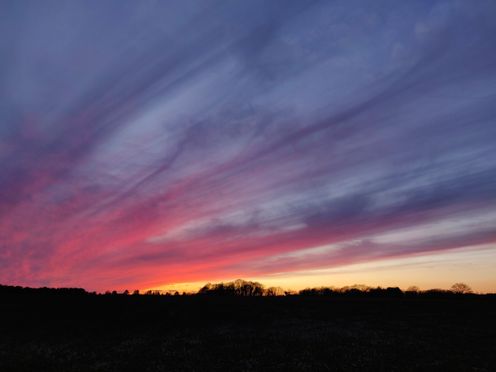 Completely black landscape creates a sharp contrast to the orange-red sky. Long clouds start from the lower left and reach the upper right like strings.