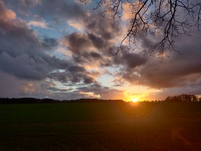 Dramatic clouded sky with a bright golden sun sitting just above the horizon.