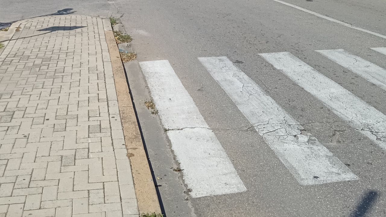 A crosswalk marked with thick white stripes, the sidewalk doesn't have a lowered (cut) curb creating an obstacle.